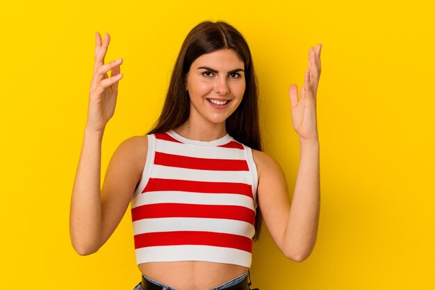 Joven mujer caucásica aislada sobre fondo amarillo celebrando una victoria o un éxito, está sorprendido y consternado.