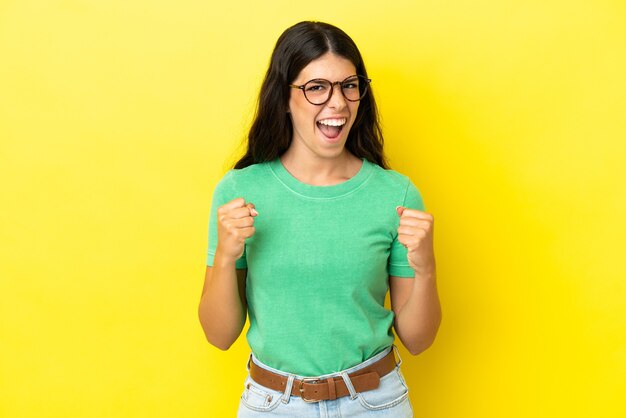 Joven mujer caucásica aislada sobre fondo amarillo celebrando una victoria en la posición ganadora