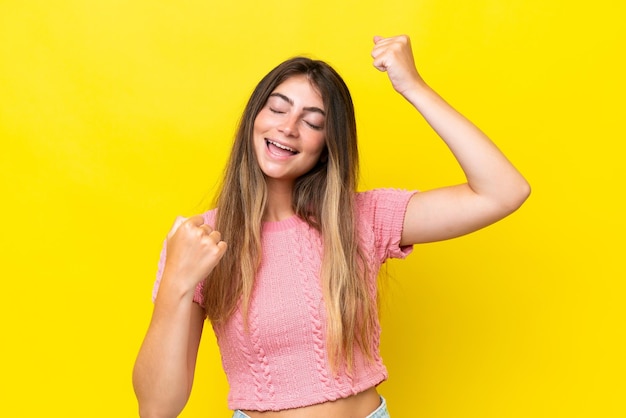 Joven mujer caucásica aislada sobre un fondo amarillo celebrando una victoria