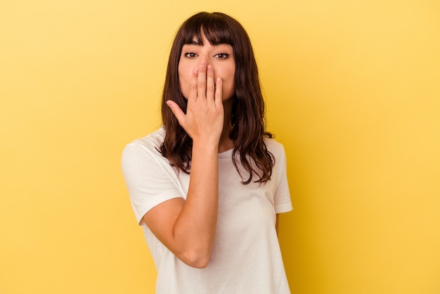 Joven mujer caucásica aislada sobre fondo amarillo conmocionada, tapándose la boca con las manos, ansiosa por descubrir algo nuevo.