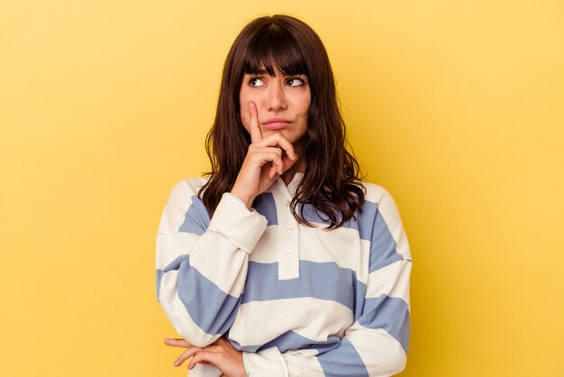 Joven mujer caucásica aislada sobre fondo amarillo contemplando, planificando una estrategia, pensando en la forma de un negocio.