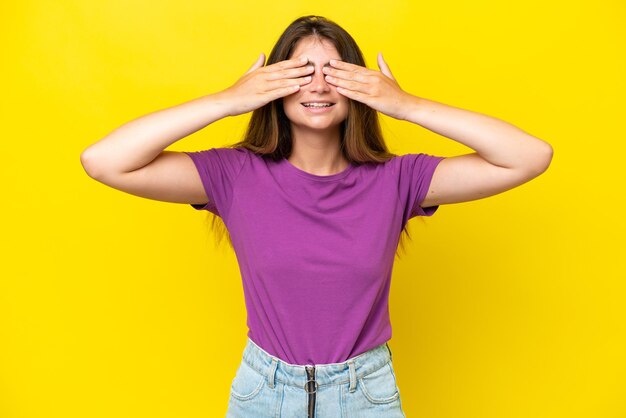 Foto joven mujer caucásica aislada sobre un fondo amarillo cubriendo los ojos con las manos y sonriendo