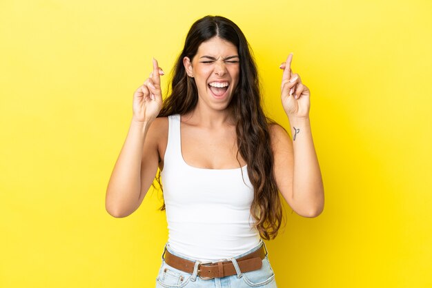 Joven mujer caucásica aislada sobre fondo amarillo con los dedos cruzando