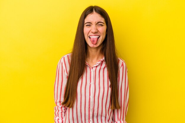 Joven mujer caucásica aislada sobre fondo amarillo divertido y amistoso sacando la lengua.