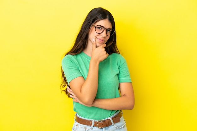 Joven mujer caucásica aislada sobre fondo amarillo con dudas