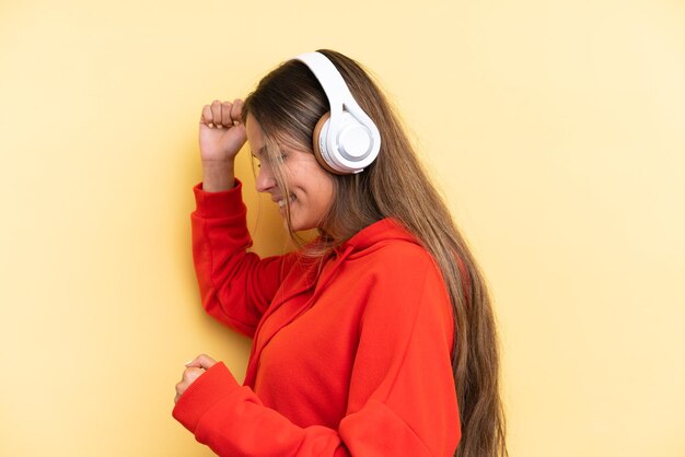 Joven mujer caucásica aislada sobre fondo amarillo escuchando música y bailando