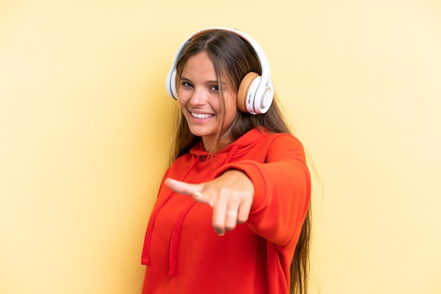 Joven mujer caucásica aislada sobre fondo amarillo escuchando música