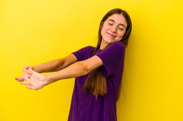 Joven mujer caucásica aislada sobre fondo amarillo estirando los brazos, posición relajada.