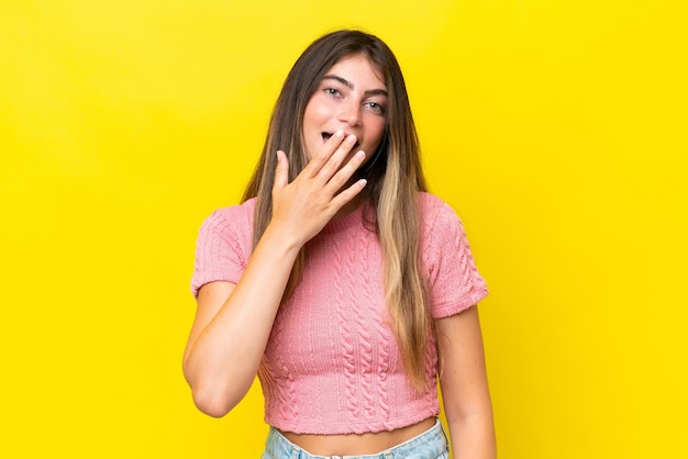 Joven mujer caucásica aislada sobre un fondo amarillo feliz y sonriente cubriendo la boca con la mano