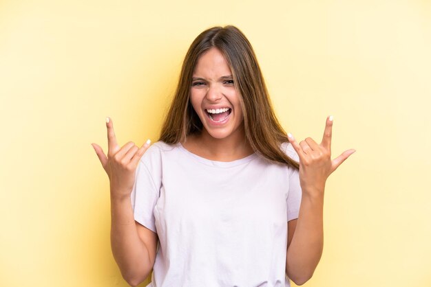 Joven mujer caucásica aislada sobre fondo amarillo haciendo gesto de cuerno