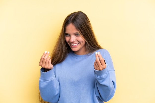 Joven mujer caucásica aislada sobre fondo amarillo haciendo gesto de dinero