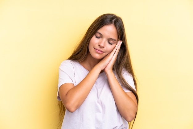 Joven mujer caucásica aislada sobre fondo amarillo haciendo gesto de sueño en expresión adorable