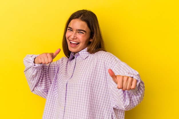 Joven mujer caucásica aislada sobre fondo amarillo levantando ambos pulgares, sonriendo y confiado.