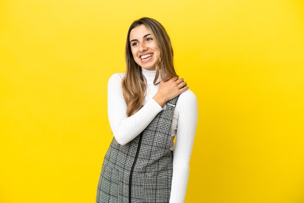 Joven mujer caucásica aislada sobre fondo amarillo mirando hacia arriba mientras sonríe