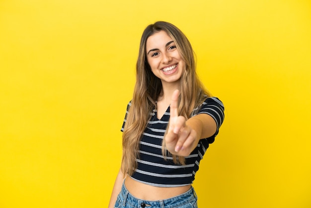 Joven mujer caucásica aislada sobre fondo amarillo mostrando y levantando un dedo