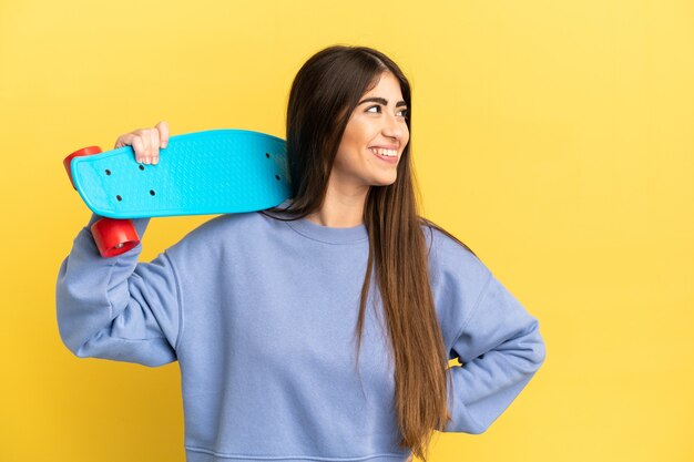 Joven mujer caucásica aislada sobre fondo amarillo con un patín