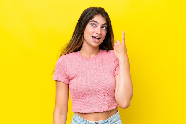 Foto joven mujer caucásica aislada sobre un fondo amarillo pensando en una idea señalando con el dedo hacia arriba