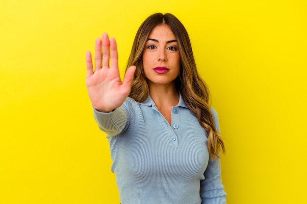 Joven mujer caucásica aislada sobre fondo amarillo de pie con la mano extendida mostrando la señal de stop, impidiéndote.