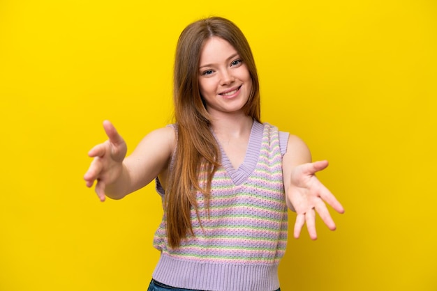 Joven mujer caucásica aislada sobre fondo amarillo presentando e invitando a venir con la mano