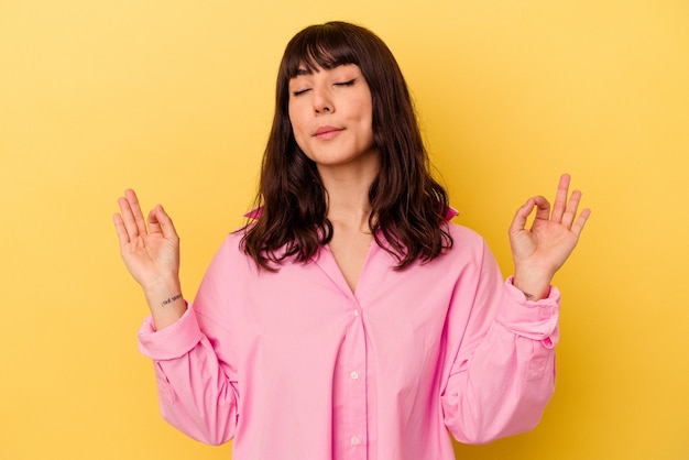 Joven mujer caucásica aislada sobre fondo amarillo se relaja después de un duro día de trabajo, ella está realizando yoga.