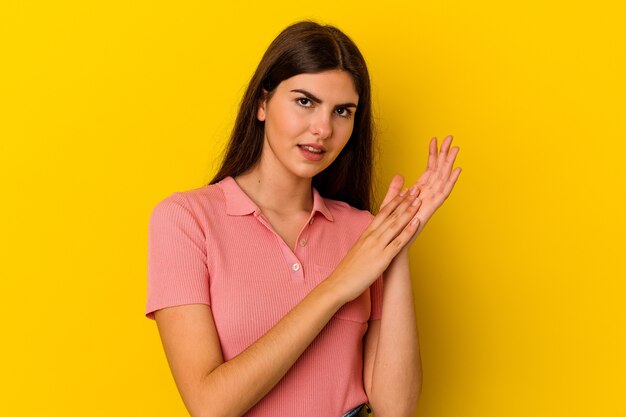 Joven mujer caucásica aislada sobre fondo amarillo sintiéndose enérgica y cómoda, frotándose las manos con confianza.