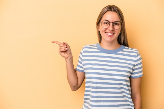 Joven mujer caucásica aislada sobre fondo amarillo sonriendo alegremente apuntando con el dedo índice.