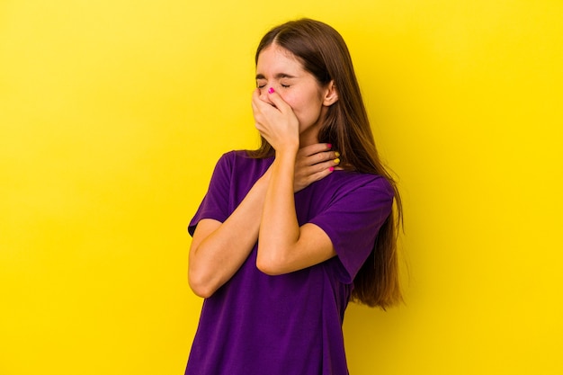 Joven mujer caucásica aislada sobre fondo amarillo sufre dolor de garganta debido a un virus o infección.