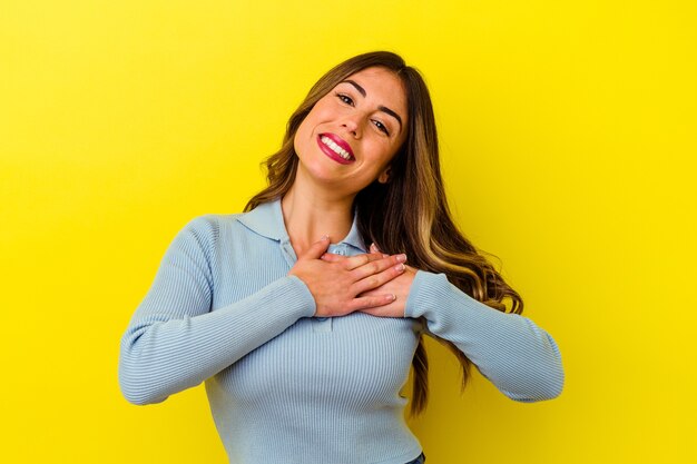 Joven mujer caucásica aislada sobre fondo amarillo tiene una expresión amistosa, presionando la palma contra el pecho. Concepto de amor.