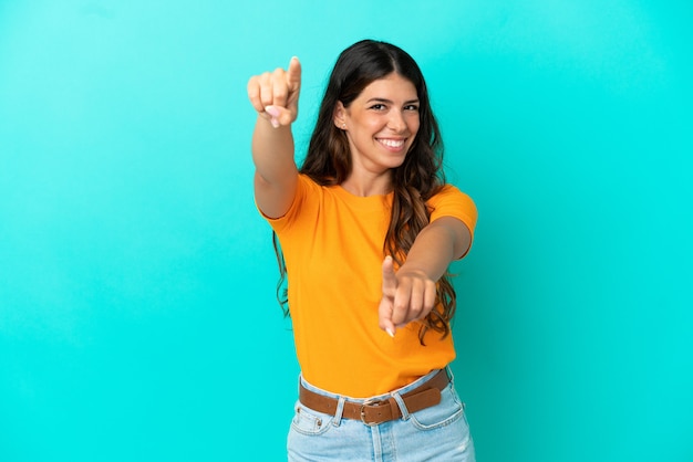 Joven mujer caucásica aislada sobre fondo azul apuntando al frente con expresión feliz