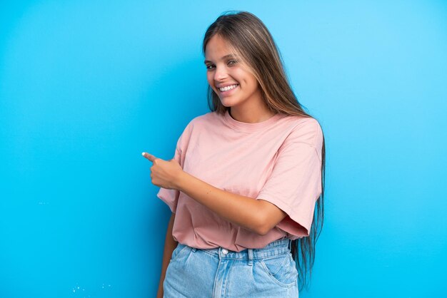 Joven mujer caucásica aislada sobre fondo azul apuntando hacia atrás