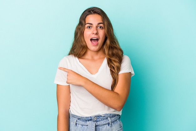 Joven mujer caucásica aislada sobre fondo azul apuntando hacia el lado