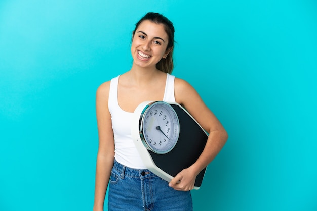 Joven mujer caucásica aislada sobre fondo azul con báscula