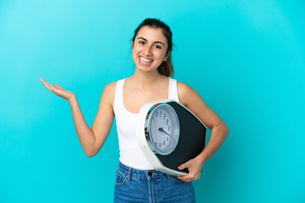 Joven mujer caucásica aislada sobre fondo azul con báscula