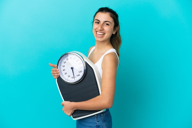 Joven mujer caucásica aislada sobre fondo azul con báscula