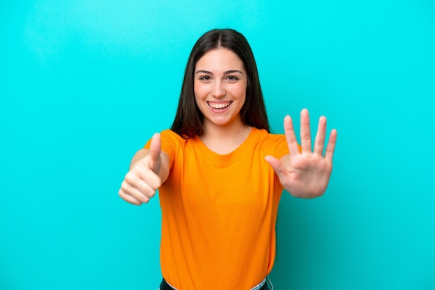 Joven mujer caucásica aislada sobre fondo azul contando seis con los dedos