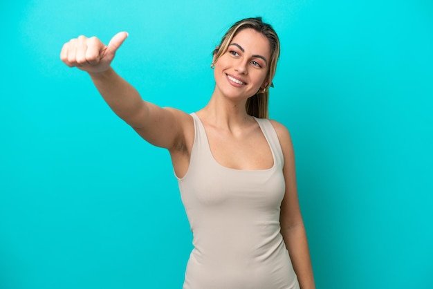 Joven mujer caucásica aislada sobre fondo azul dando un pulgar hacia arriba gesto