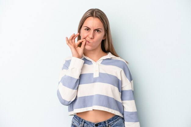 Joven mujer caucásica aislada sobre fondo azul con los dedos en los labios guardando un secreto.