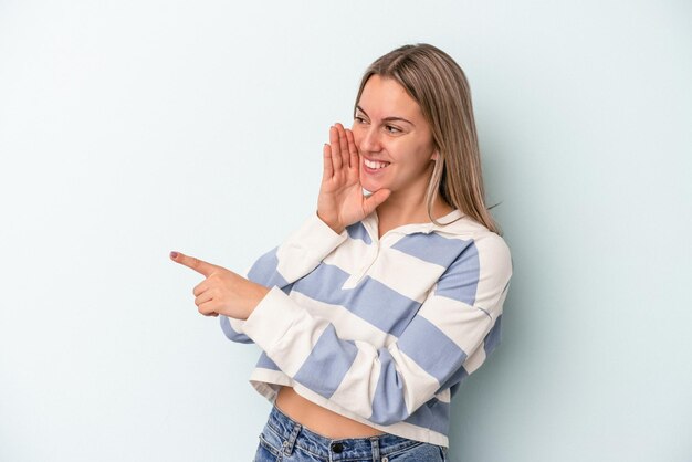 Joven mujer caucásica aislada sobre fondo azul diciendo un chisme, apuntando al lado informando algo.