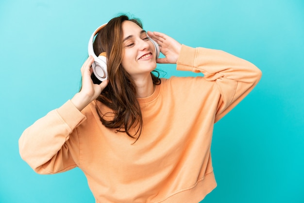 Joven mujer caucásica aislada sobre fondo azul escuchando música y cantando