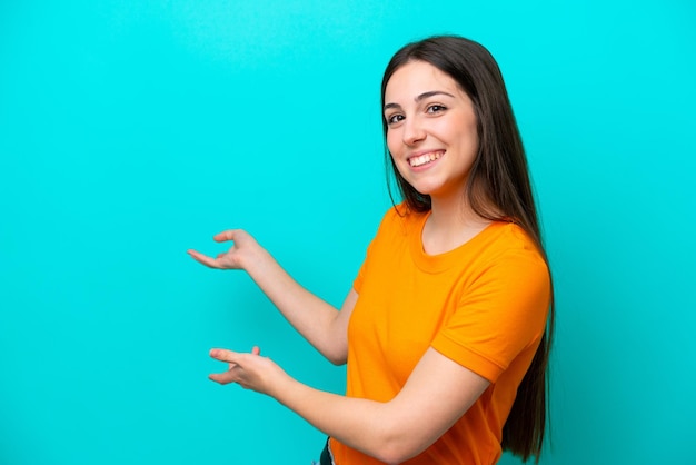 Joven mujer caucásica aislada sobre fondo azul extendiendo las manos hacia el lado para invitar a venir