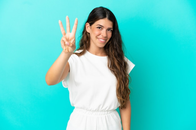 Joven mujer caucásica aislada sobre fondo azul feliz y contando tres con los dedos