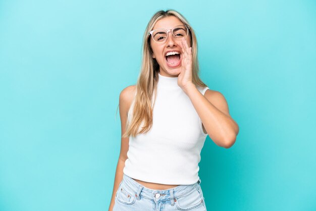 Joven mujer caucásica aislada sobre fondo azul gritando con la boca abierta