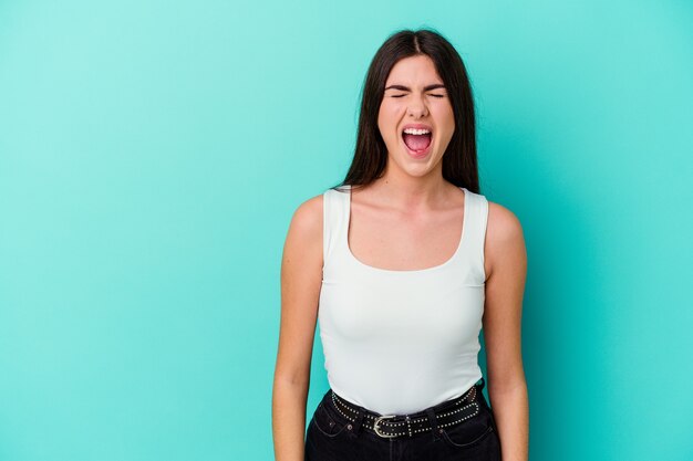 Joven mujer caucásica aislada sobre fondo azul gritando muy enojado, concepto de rabia, frustrado.