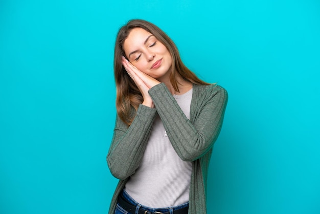 Joven mujer caucásica aislada sobre fondo azul haciendo gesto de sueño en expresión adorable