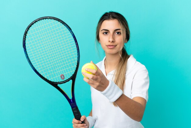 Joven mujer caucásica aislada sobre fondo azul jugando al tenis