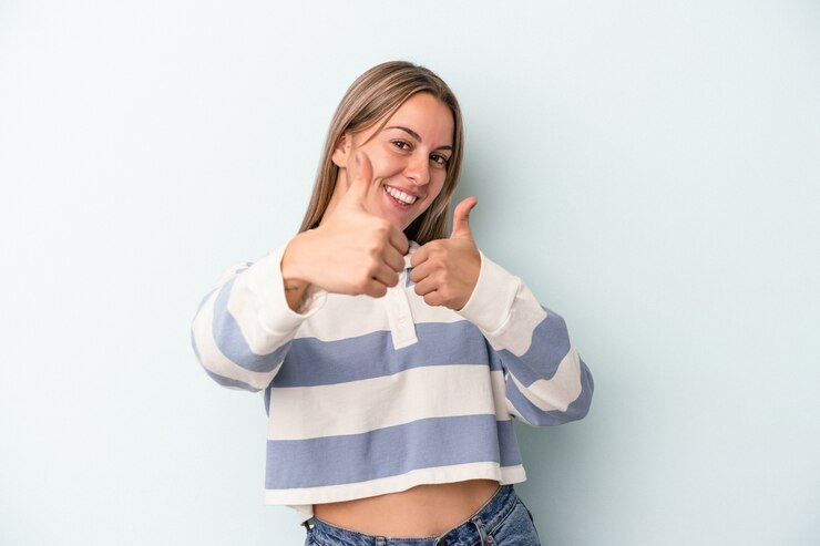 Foto joven mujer caucásica aislada sobre fondo azul levantando ambos pulgares, sonriendo y confiado.
