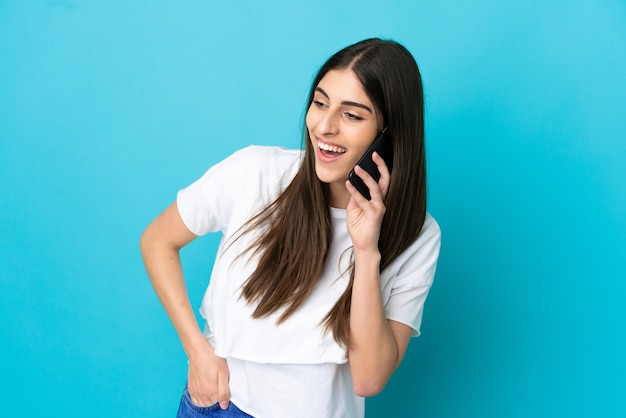 Joven mujer caucásica aislada sobre fondo azul manteniendo una conversación con el teléfono móvil con alguien