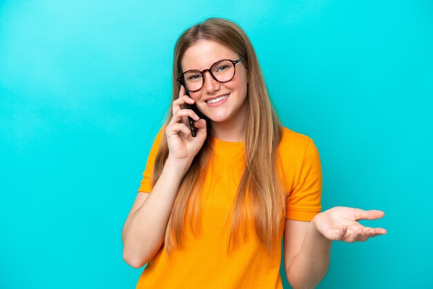 Joven mujer caucásica aislada sobre fondo azul manteniendo una conversación con el teléfono móvil con alguien