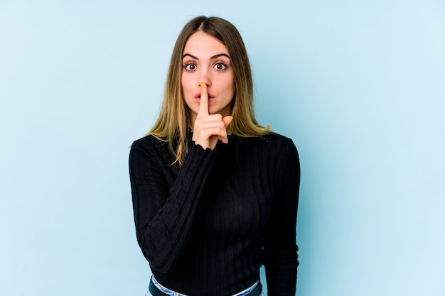 Joven mujer caucásica aislada sobre fondo azul manteniendo un secreto o pidiendo silencio.