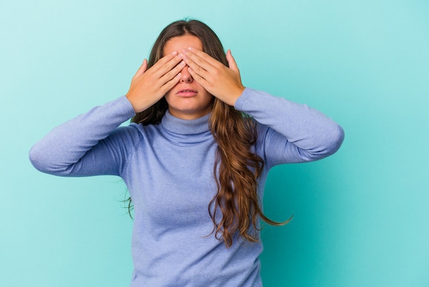 Joven mujer caucásica aislada sobre fondo azul miedo cubrirse los ojos con las manos.